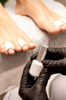 White nail polish in the hands of a manicurist while painting nails on a female feet, closeup