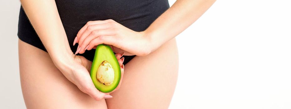 Healthy nutrition and pregnancy concept. Young woman holding one half of an avocado fruit close to her belly over a white background