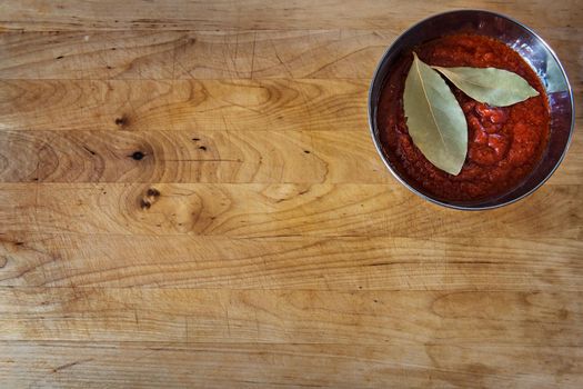old wooden board with tomato sauce and bay leaves in a bowl. Flat lay, top view with copy space