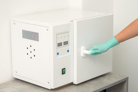 Beautician in protective gloves close the door of the machine for disinfection of tools before the medical procedures