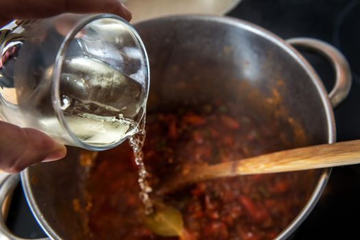 closeup, pouring white wine into the vegetable garnish that is cooking in the pot, there is a wooden spoon. Background with lens blur