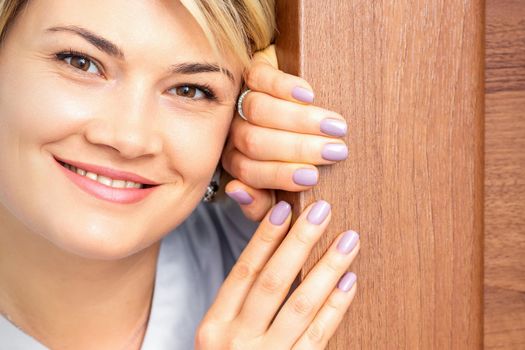Close up portrait of the young smiling caucasian woman looks out from behind the door looking at the camera