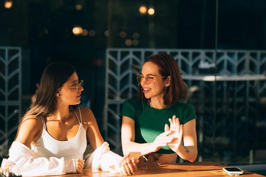 Two excited young girls using mobile phones while sitting at the cafe outdoors