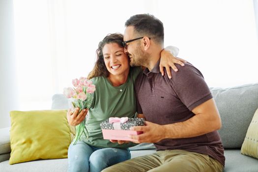Smiling woman and boyfriend for giving her a present at home