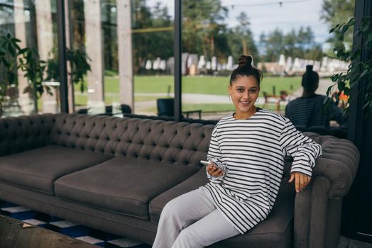 Happy casual beautiful woman with a phone sitting on a sofa at home.