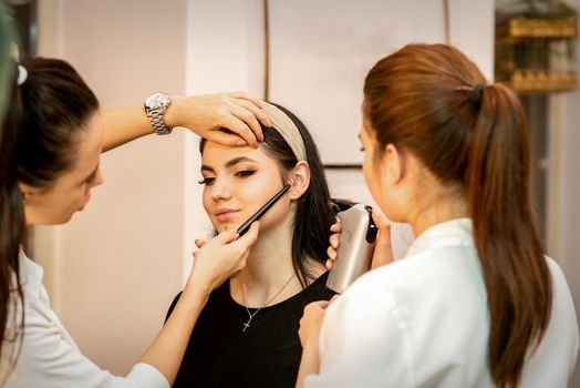 Makeup artist using an airbrush on the face of a young caucasian woman in a beauty salon