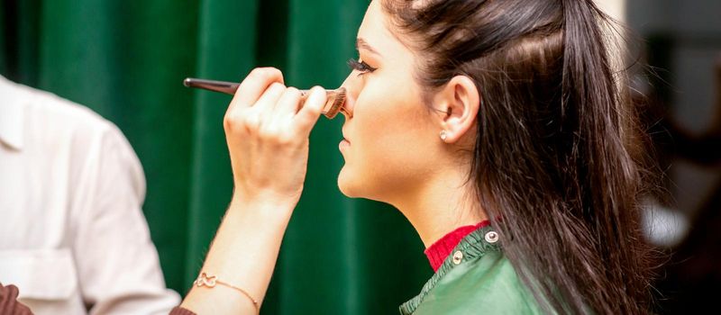 The face of the young woman receives powder on her nose with a brush with the hand of a makeup artist