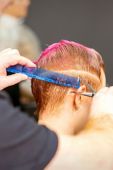 Haircut of dyed short pink wet hair of young caucasian woman by a male hairdresser in a barbershop