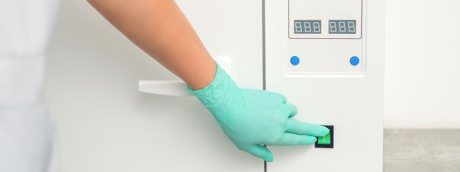 Beautician in protective gloves starts the machine for disinfection of tools before the medical procedure