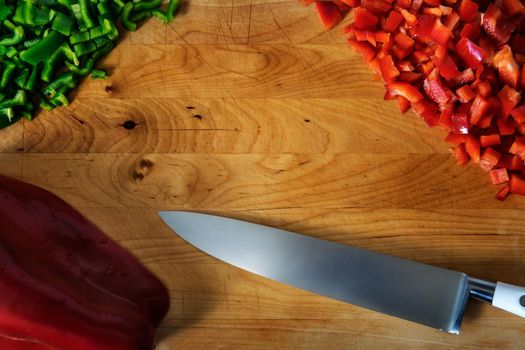 Old cutting board with a chef knife, green and red pepper chopped. Flat top view with frame style and copy space