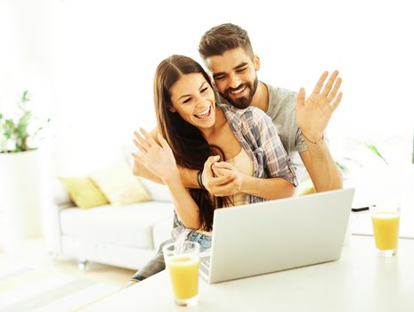 Beautiful young couple having video call on laptop computer at home