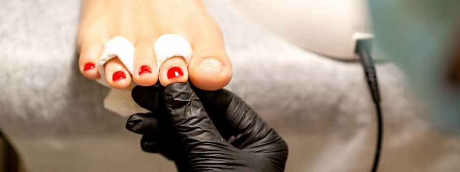 Nail painting process. A manicure master hand holds red painted fingernails on a female leg in a beauty salon