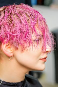 Beautiful young caucasian woman receiving new short pink hairstyle in hairdresser salon