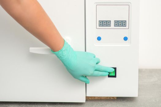 Beautician in protective gloves starts the machine for disinfection of tools before the medical procedure