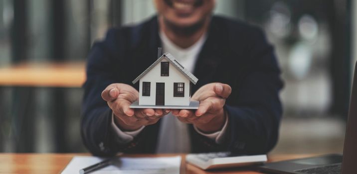 Business man hands holding modern house, House model with agent and customer discussing for contract to buy, get insurance or loan mortgage crisis real estate or property..