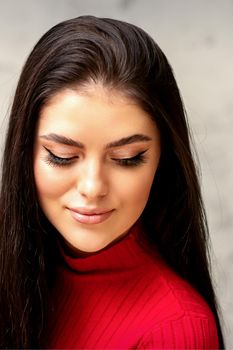 The fashionable young woman. Portrait of the beautiful female model with long hair and makeup with eyelash extensions. Beauty young woman with a black hairstyle on the background of a gray wall