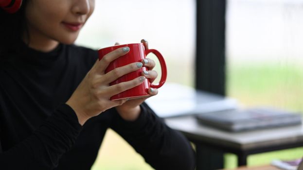 Cropped shot young woman holding red cup of hot coffee.