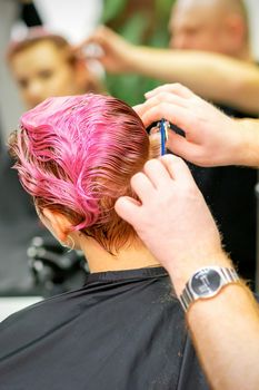 Haircut of dyed short pink wet hair of young caucasian woman by a male hairdresser in a barbershop