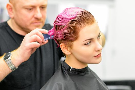 Haircut of dyed short pink wet hair of young caucasian woman by a male hairdresser in a barbershop