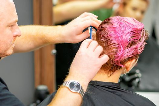 Haircut of dyed short pink wet hair of young caucasian woman by a male hairdresser in a barbershop