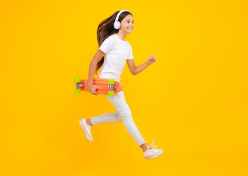 Happy teenager portrait. Jump and run. Fashion teenage lifestyle, beautiful teen girl with skateboard and headphones isolated on studio background. Smiling girl