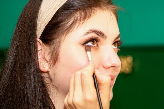 Make-up in the process. The hand of the makeup artist applies eye shadow under the eyes of a young beautiful caucasian model woman