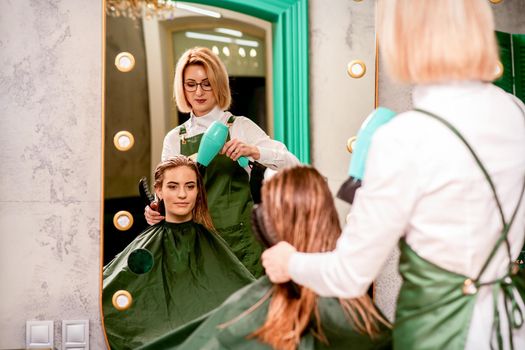 The hairdresser dries hair with a hairdryer of the beautiful young caucasian woman in the beauty salon