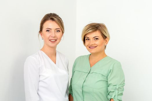 Close-up portrait of two young smiling female caucasian healthcare workers standing staring at the camera on white background
