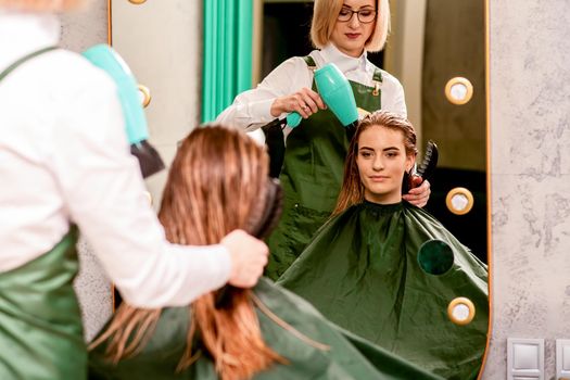 The hairdresser dries hair with a hairdryer of the beautiful young caucasian woman in the beauty salon