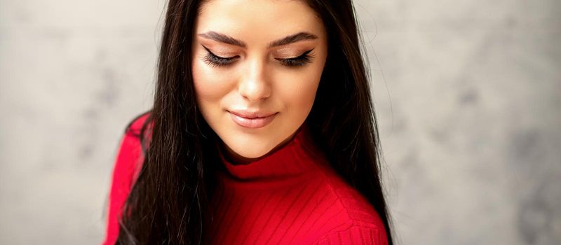 The fashionable young woman. Portrait of the beautiful female model with long hair and makeup with eyelash extensions. Beauty young woman with a black hairstyle on the background of a gray wall