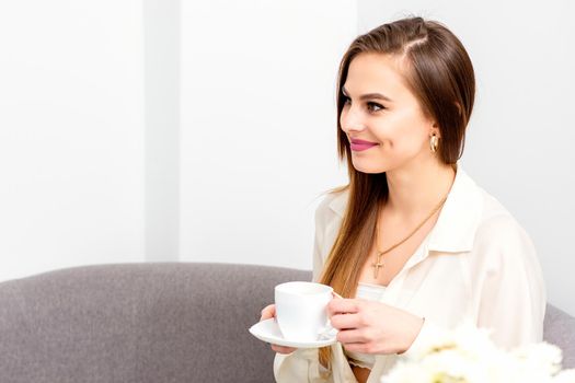 Female caucasian client with a cup of coffee in his hands smiling at a doctor's appointment