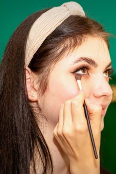 Make-up in the process. The hand of the makeup artist applies eye shadow under the eyes of a young beautiful caucasian model woman