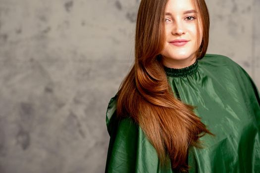 The fashionable young woman. Portrait of the beautiful female model with long hair and makeup. Beauty young caucasian woman with a brown curly hairstyle on the background of a gray wall