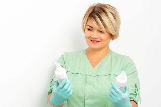 Cosmetics creams and skin care products in the hands of the female beautician smiling and standing over the white wall background