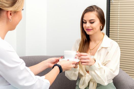 The female cosmetologist doctor treats his patient to a cup of coffee in a medical office