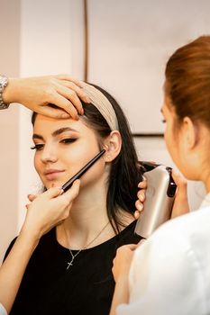 Makeup artist using an airbrush on the face of a young caucasian woman in a beauty salon