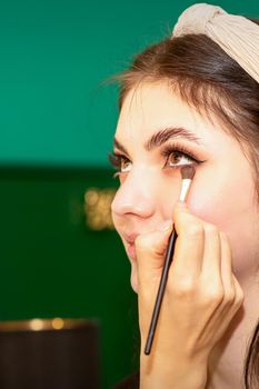 Make-up in the process. The hand of the makeup artist applies eye shadow under the eyes of a young beautiful caucasian model woman