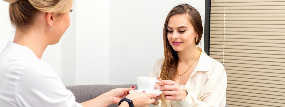 The female cosmetologist doctor treats his patient to a cup of coffee in a medical office