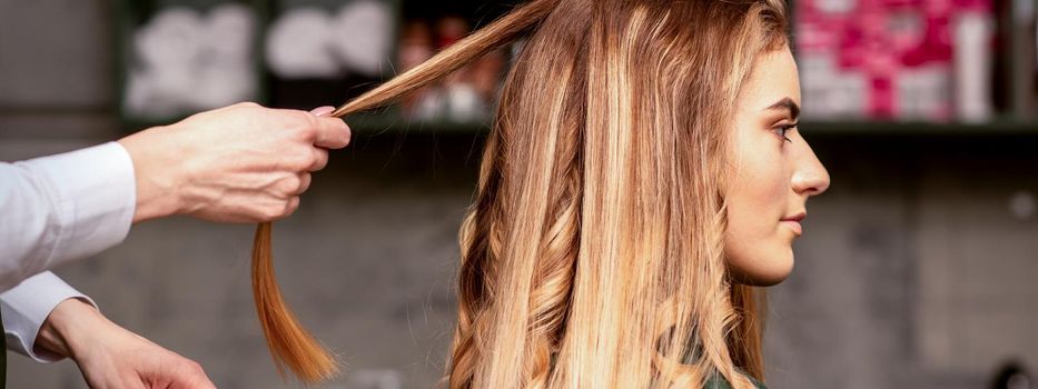 Professional hair care. Beautiful young caucasian blonde woman with long hair receiving hairstyling in a beauty salon