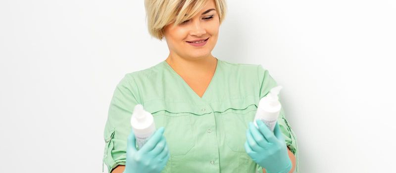 Cosmetics creams and skin care products in the hands of the female beautician smiling and standing over the white wall background