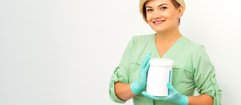 Cosmetics creams and skin care products in the hands of the female beautician smiling and standing over the white wall background