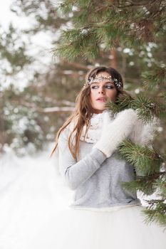 Beautiful bride in a white dress with a bouquet in a snow-covered winter forest. Portrait of the bride in nature.