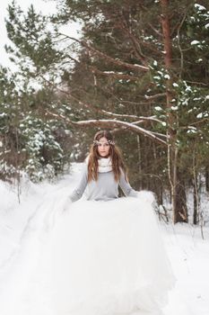 Beautiful bride in a white dress with a bouquet in a snow-covered winter forest. Portrait of the bride in nature.