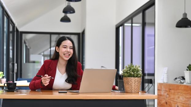 Cheerful businesswoman sitting at her workplace and working with laptop computer.