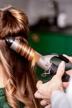 The female hairdresser is curling hair for a brown-haired young caucasian woman in a beauty salon