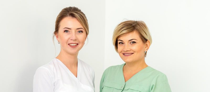 Close-up portrait of two young smiling female caucasian healthcare workers standing staring at the camera on white background