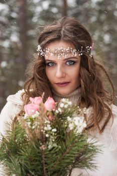 Beautiful bride in a white dress with a bouquet in a snow-covered winter forest. Portrait of the bride in nature.