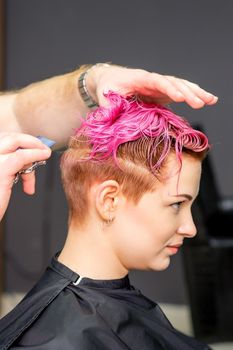 Haircut of dyed short pink wet hair of young caucasian woman by a male hairdresser in a barbershop