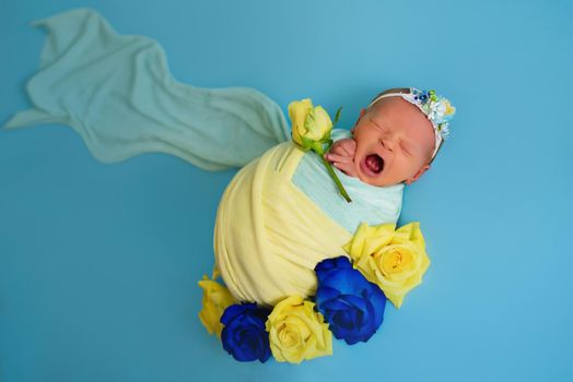 Ukrainian newborn crying in the studio patriotic blue yellow colors during the war in Ukraine 2022. A little baby, girl sleeps on isolated background