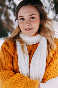 Teen blonde in a yellow sweater outside in winter. A teenage girl on a walk in winter clothes in a snowy forest.